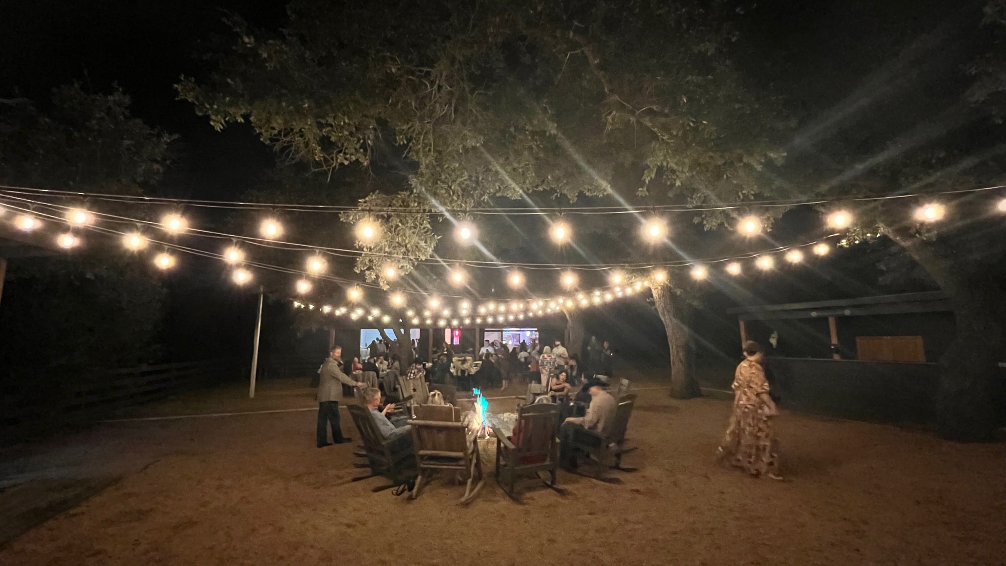 Guests gathered around the fire pit under string lights in the grove at Willow Sky Ranch